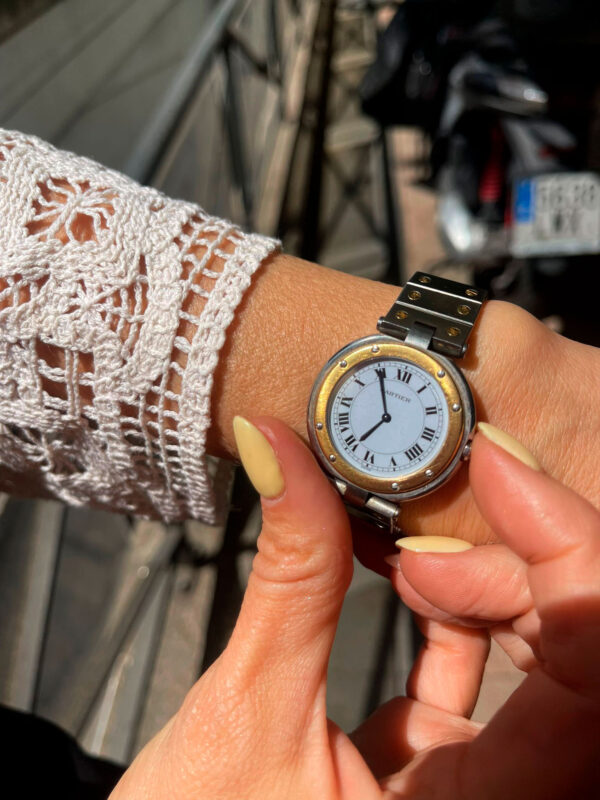 Modelo mostrando en la mano el icónico reloj Ronde con números romanos, elegantes agujas azules en forma de espada y distintivo cabujón de zafiro.