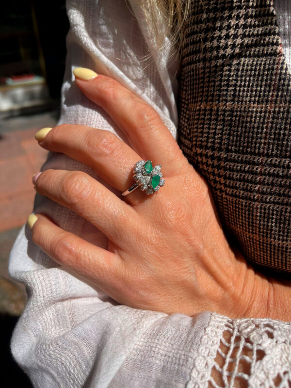 Modelo posando con una sofisticada sortija de esmeralda y diamantes, con una esmeralda central dividida en delicados pétalos que realzan su diseño exclusivo.